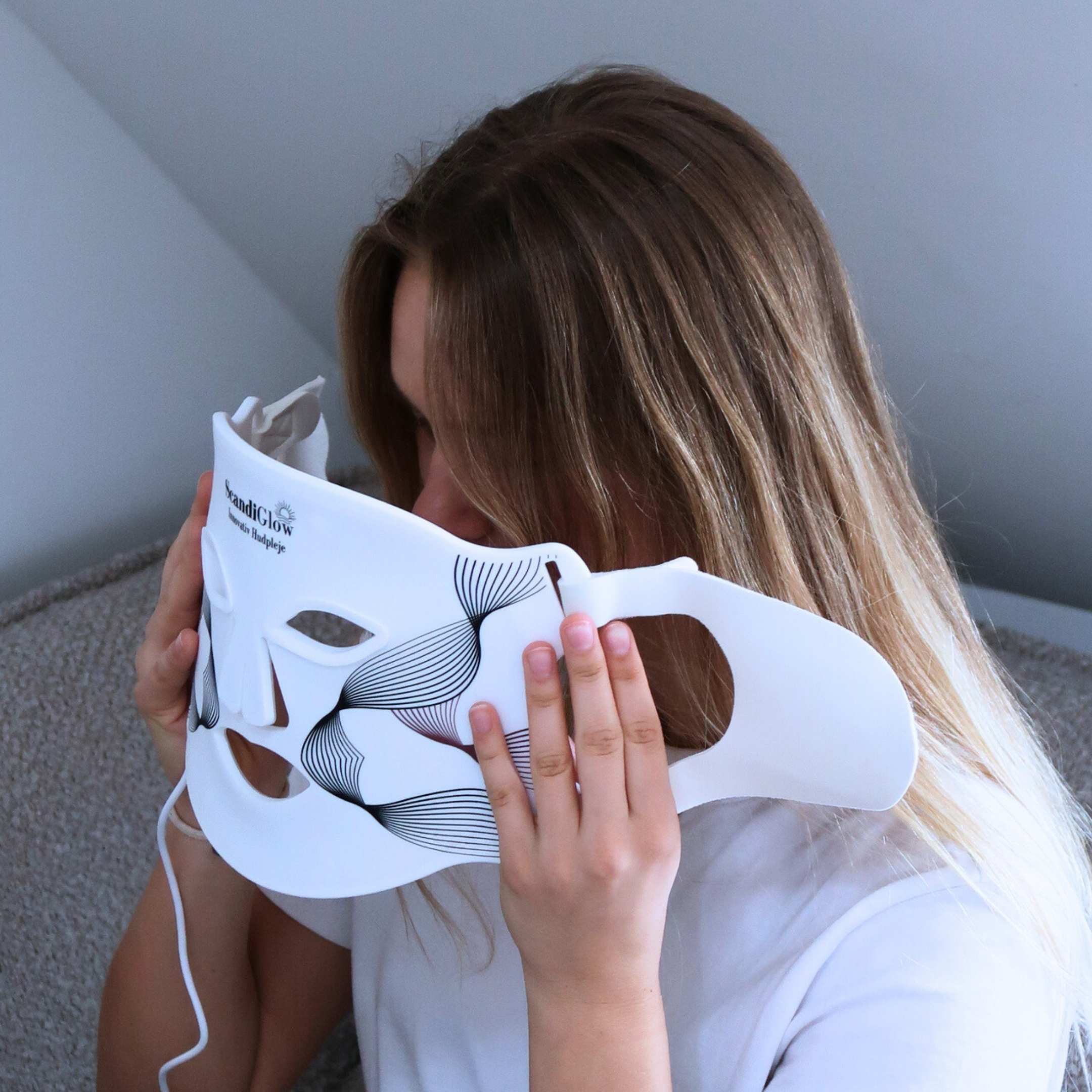 Kvinde holder ScandiGlow LED lysterapi maske foran ansigtet.